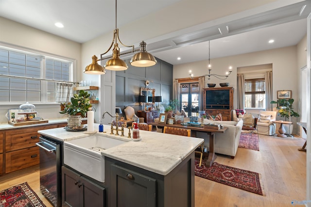 kitchen featuring light stone counters, hanging light fixtures, sink, a center island with sink, and light hardwood / wood-style floors