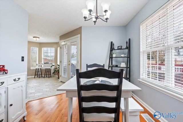dining room featuring a textured ceiling, visible vents, light wood-style flooring, baseboards, and an inviting chandelier