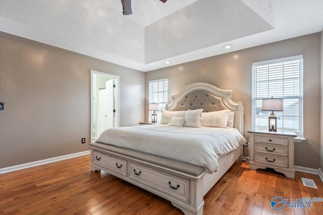 bedroom with a tray ceiling, baseboards, connected bathroom, light wood-style floors, and visible vents