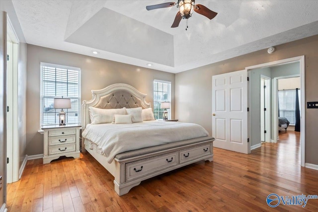 bedroom with a tray ceiling, vaulted ceiling, baseboards, a textured ceiling, and light wood-style flooring