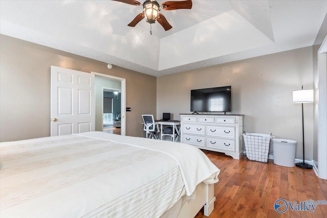 bedroom with hardwood / wood-style floors, baseboards, a ceiling fan, and a raised ceiling