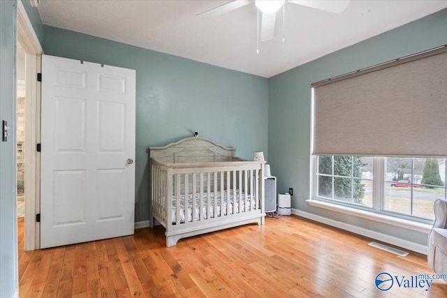 bedroom with a nursery area, baseboards, visible vents, and wood-type flooring