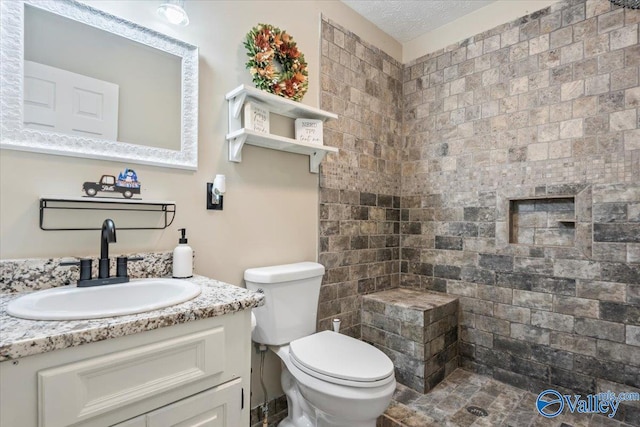 bathroom featuring a textured ceiling, toilet, tiled shower, and vanity
