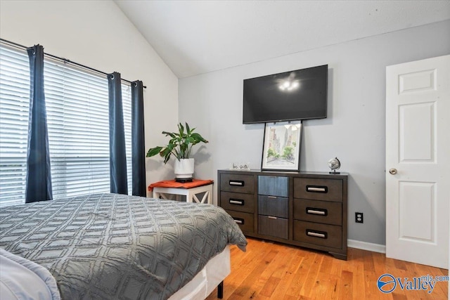 bedroom with light wood finished floors, baseboards, and lofted ceiling