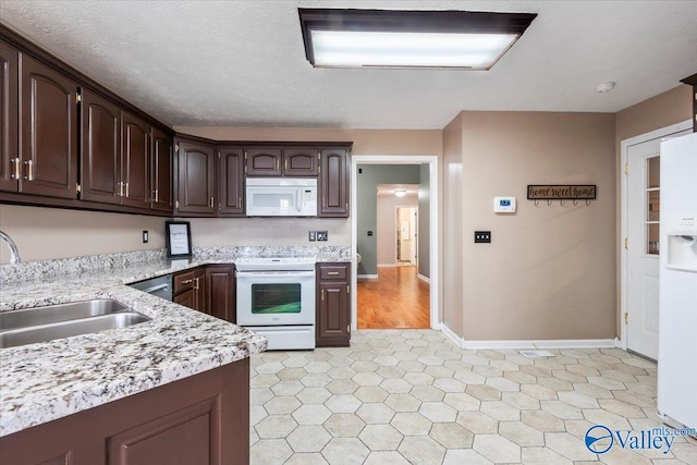 kitchen featuring a textured ceiling, white appliances, baseboards, dark brown cabinets, and a sink