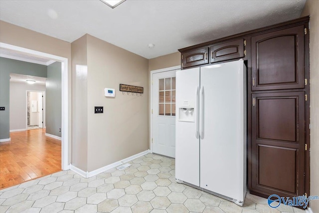 kitchen featuring baseboards, dark brown cabinets, and white fridge with ice dispenser