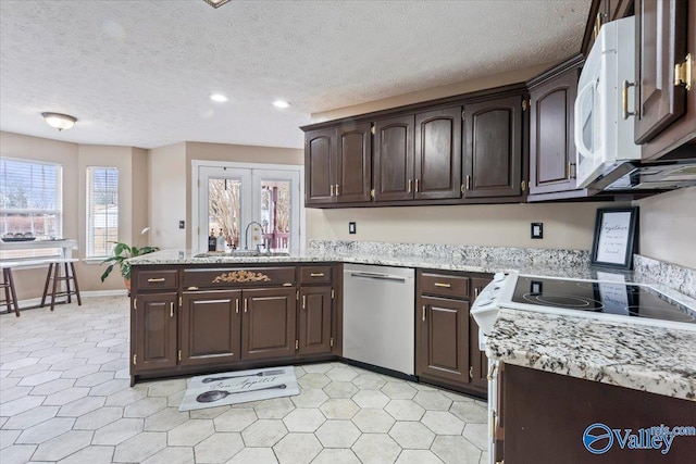 kitchen with dark brown cabinetry, a sink, a peninsula, and white appliances