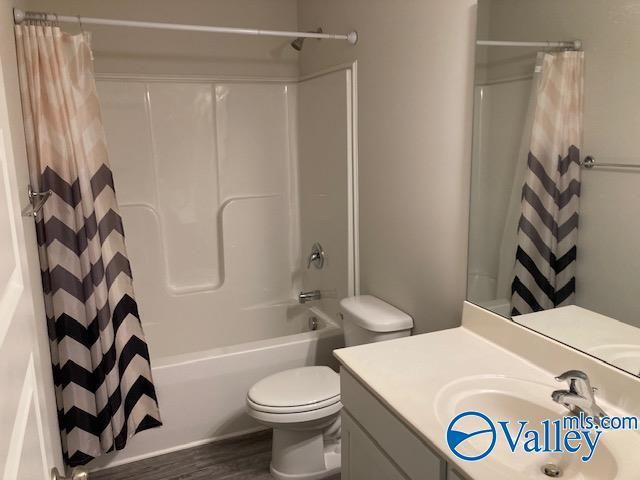 bathroom with wood finished floors, vanity, toilet, and shower / tub combo with curtain