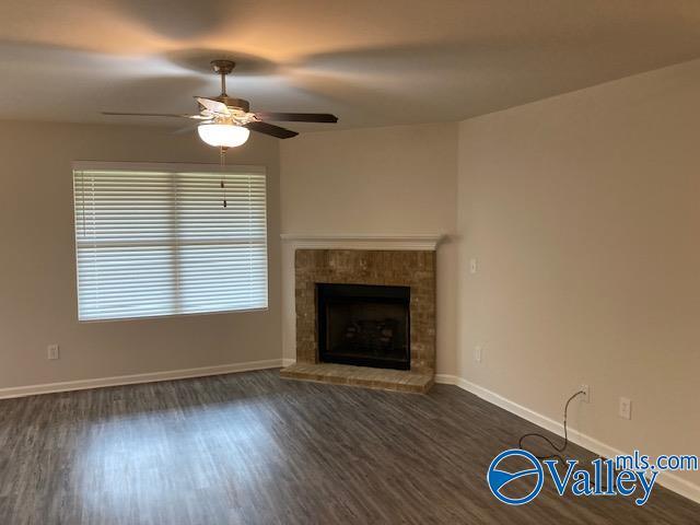 unfurnished living room with baseboards, wood finished floors, a ceiling fan, and a brick fireplace