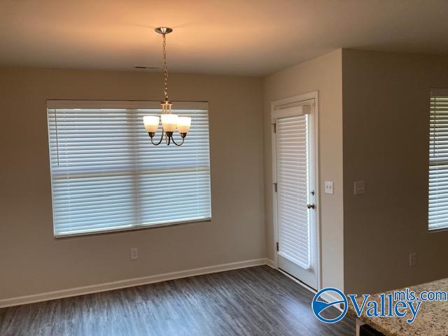 unfurnished dining area featuring baseboards, wood finished floors, a notable chandelier, and a wealth of natural light