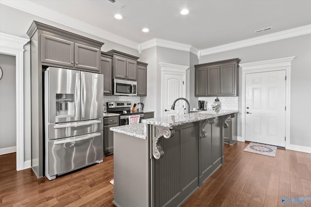 kitchen featuring appliances with stainless steel finishes, a kitchen breakfast bar, light stone counters, dark hardwood / wood-style floors, and an island with sink