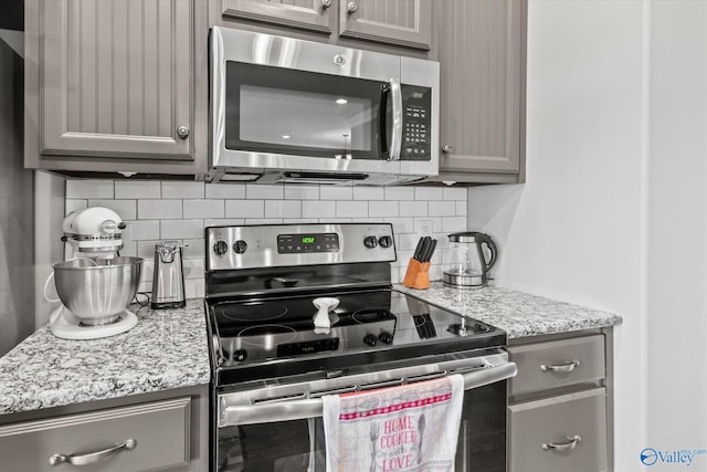 kitchen with stainless steel appliances, light stone counters, tasteful backsplash, and gray cabinetry