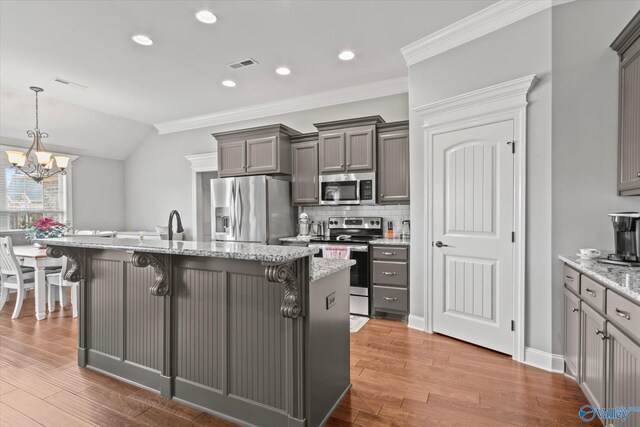 kitchen with hardwood / wood-style floors, appliances with stainless steel finishes, light stone counters, a breakfast bar area, and a chandelier