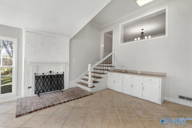 unfurnished living room with light tile patterned floors, visible vents, stairway, ornamental molding, and a brick fireplace