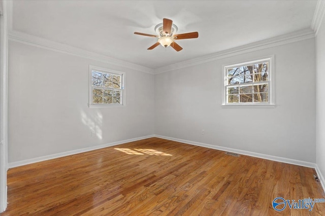 spare room featuring crown molding, baseboards, a wealth of natural light, and wood finished floors