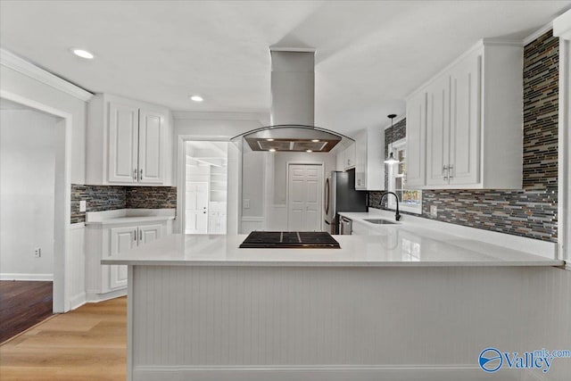 kitchen featuring a peninsula, a sink, white cabinets, light countertops, and island exhaust hood