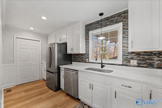 kitchen featuring white cabinets, appliances with stainless steel finishes, light countertops, light wood-style floors, and a sink