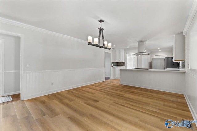 unfurnished living room with light wood-style floors, crown molding, a chandelier, and a wainscoted wall