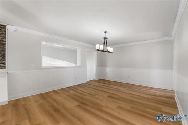 unfurnished room featuring an inviting chandelier, wood finished floors, and wainscoting