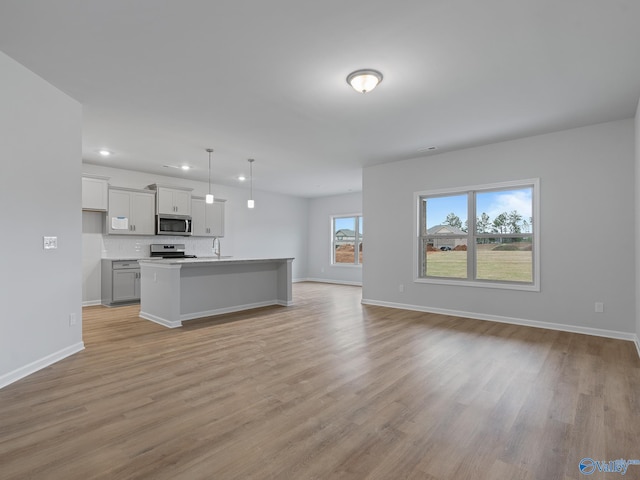 kitchen featuring light hardwood / wood-style floors, sink, stainless steel appliances, a center island with sink, and decorative light fixtures