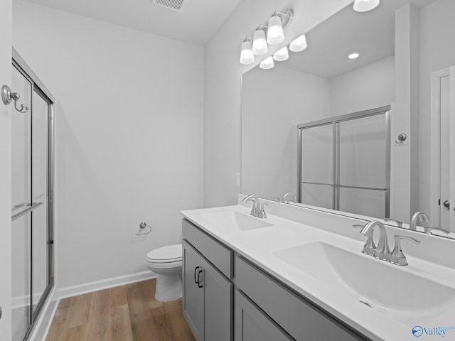 bathroom with hardwood / wood-style floors, a shower with door, toilet, and vanity