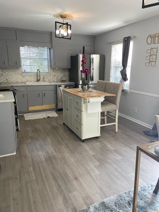 kitchen featuring butcher block counters, a center island, sink, stainless steel appliances, and gray cabinets