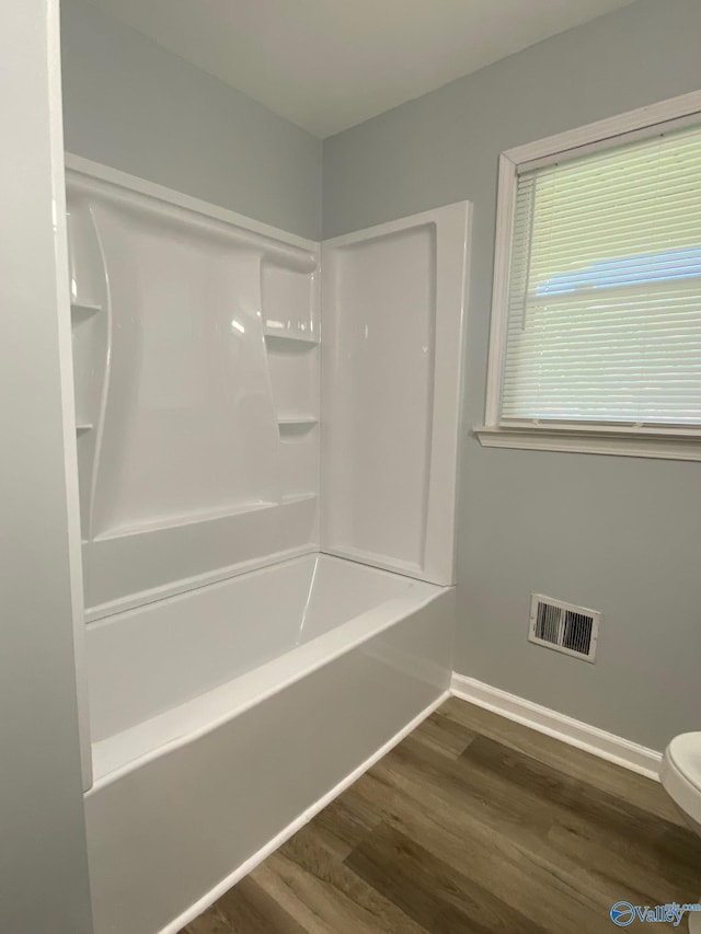 bathroom with wood-type flooring,  shower combination, and toilet