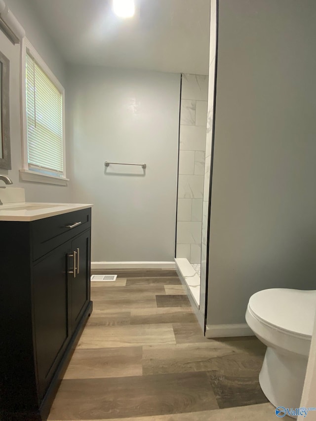 bathroom with toilet, tiled shower, wood-type flooring, and vanity