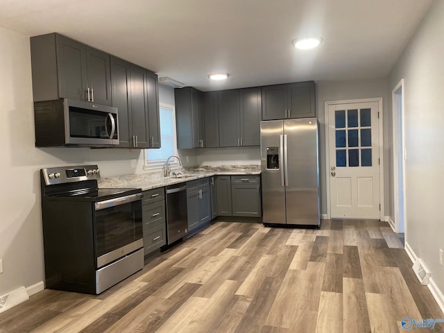 kitchen with stainless steel appliances, light stone countertops, light hardwood / wood-style floors, gray cabinets, and sink