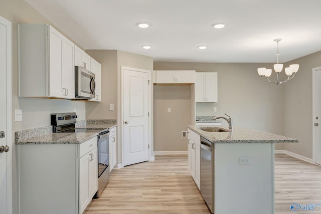 kitchen with light wood finished floors, light stone countertops, stainless steel appliances, white cabinetry, and a sink