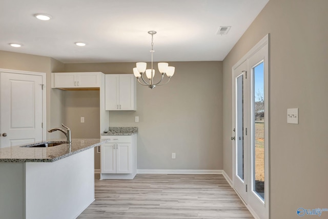 kitchen with visible vents, light stone countertops, an inviting chandelier, white cabinets, and a sink