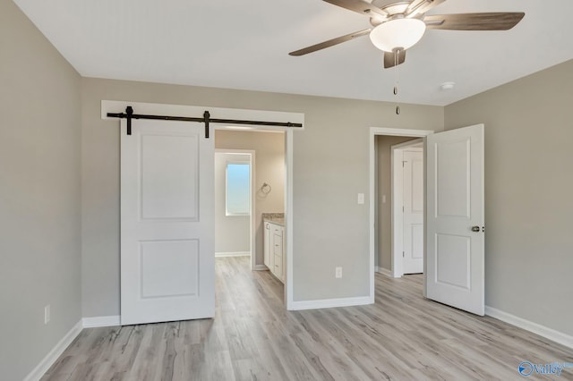 unfurnished bedroom featuring a barn door, light wood-style flooring, and baseboards