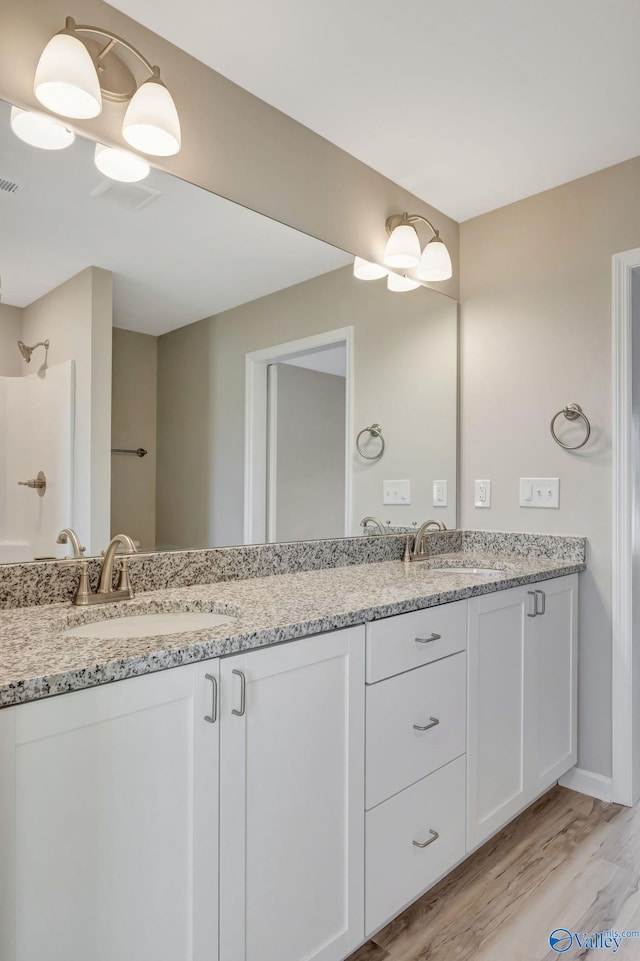 full bathroom featuring double vanity, visible vents, wood finished floors, and a sink