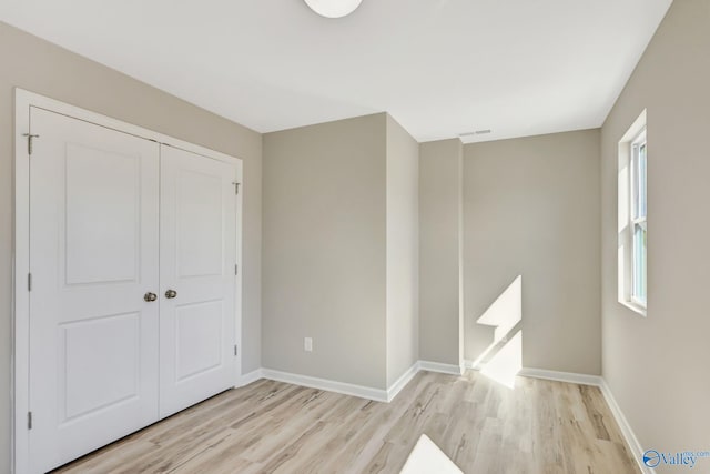 unfurnished bedroom with light wood-style flooring, visible vents, baseboards, and a closet