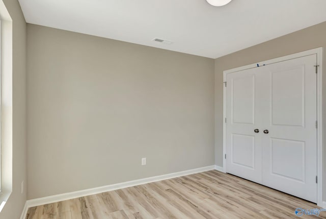 unfurnished bedroom with a closet, baseboards, light wood-style floors, and visible vents