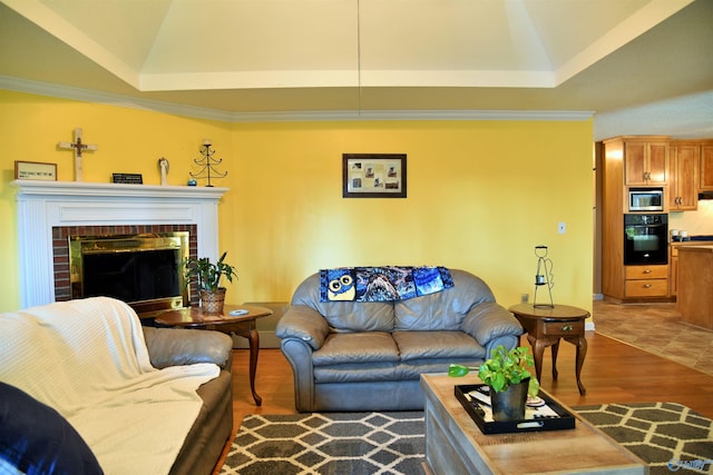 living room featuring a brick fireplace, a tray ceiling, and hardwood / wood-style flooring