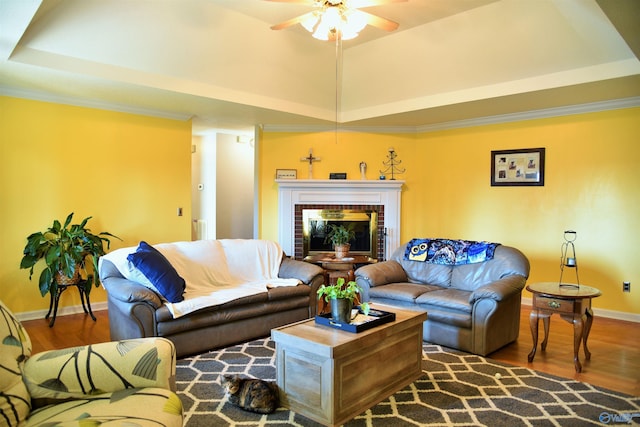 living room featuring a raised ceiling, wood-type flooring, crown molding, and ceiling fan