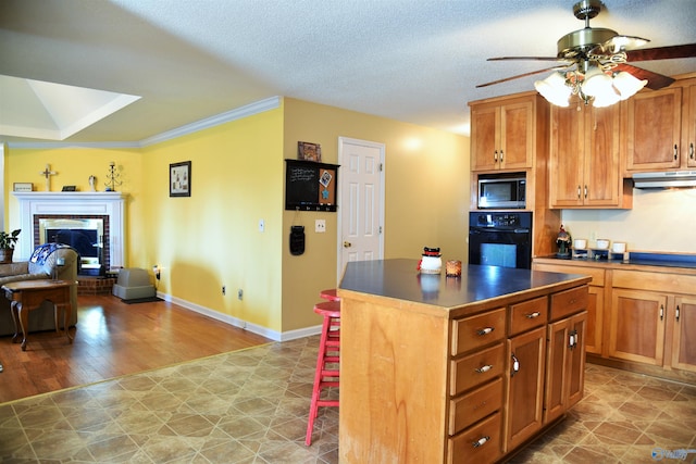 kitchen featuring ceiling fan, a fireplace, a kitchen island, crown molding, and black appliances