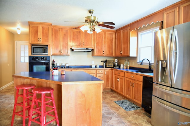 kitchen featuring ceiling fan, a kitchen island, black appliances, a kitchen bar, and sink