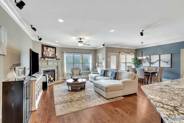 living area with recessed lighting, crown molding, a stone fireplace, and hardwood / wood-style flooring