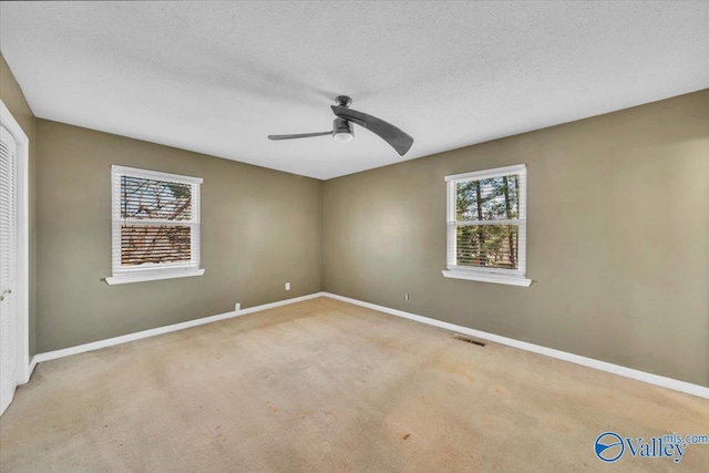 carpeted empty room with visible vents, ceiling fan, a textured ceiling, and baseboards