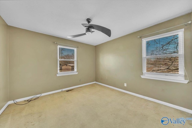 carpeted spare room with baseboards, visible vents, and ceiling fan