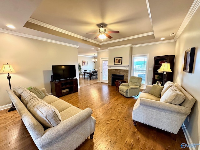 living room with a fireplace, a tray ceiling, wood-type flooring, and ceiling fan with notable chandelier