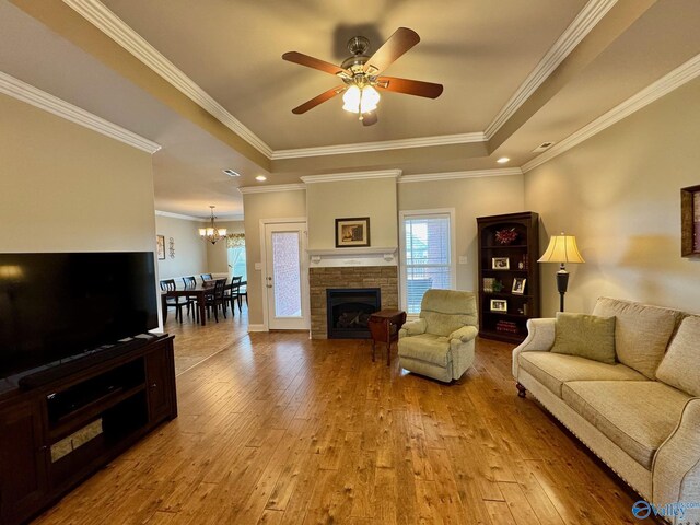 living room featuring a tray ceiling, a stone fireplace, light hardwood / wood-style floors, and ceiling fan with notable chandelier