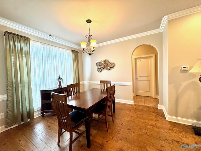 dining area with wood-type flooring, ornamental molding, and a chandelier