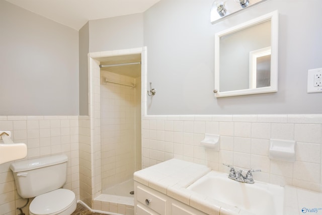 bathroom with a tile shower, vanity, tile walls, and toilet