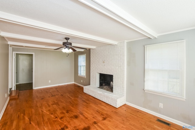 unfurnished living room with a fireplace, beamed ceiling, wood-type flooring, crown molding, and ceiling fan