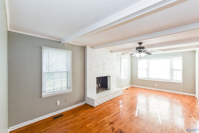 unfurnished living room with ceiling fan, ornamental molding, beam ceiling, a brick fireplace, and light hardwood / wood-style flooring