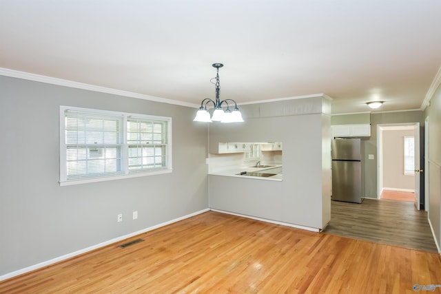 unfurnished room with an inviting chandelier, light wood-type flooring, and ornamental molding