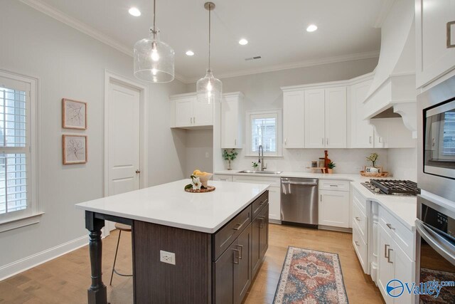 kitchen with appliances with stainless steel finishes, white cabinetry, a kitchen island, and sink